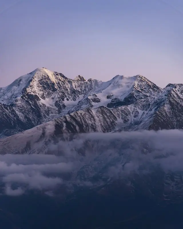 Snow-capped mountains emerge from misty clouds at dawn