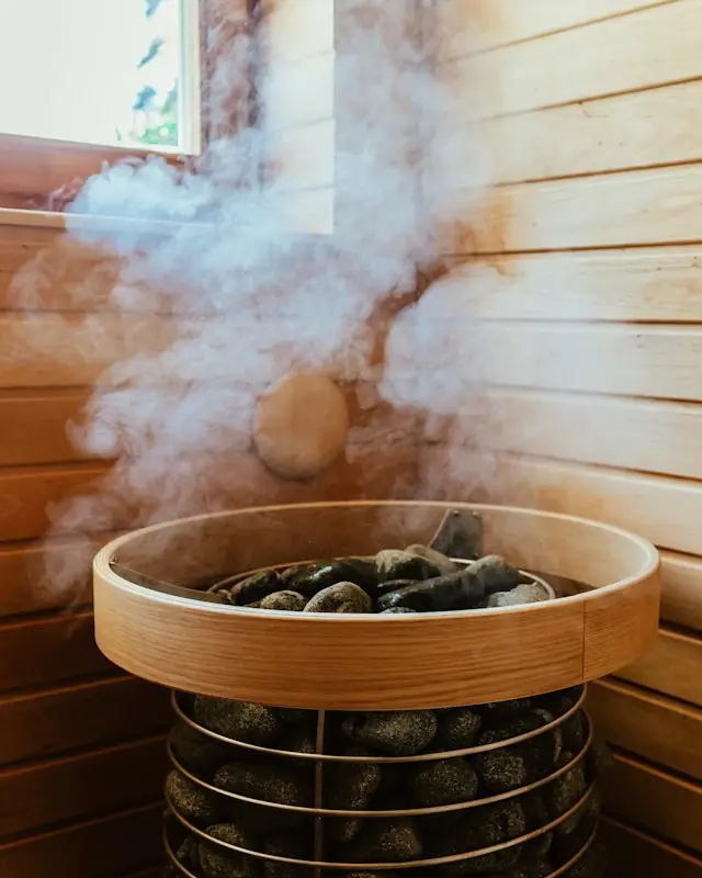 Steam rising from hot dark stones in a wooden sauna heater
