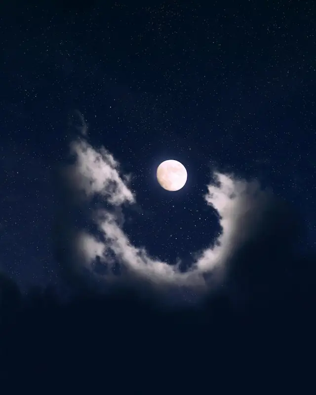 A bright full moon surrounded by dark clouds in a starry night sky