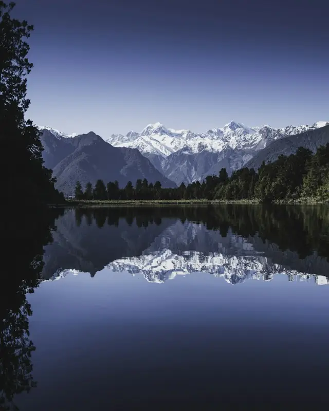 Body of water between green trees under clear blue sky